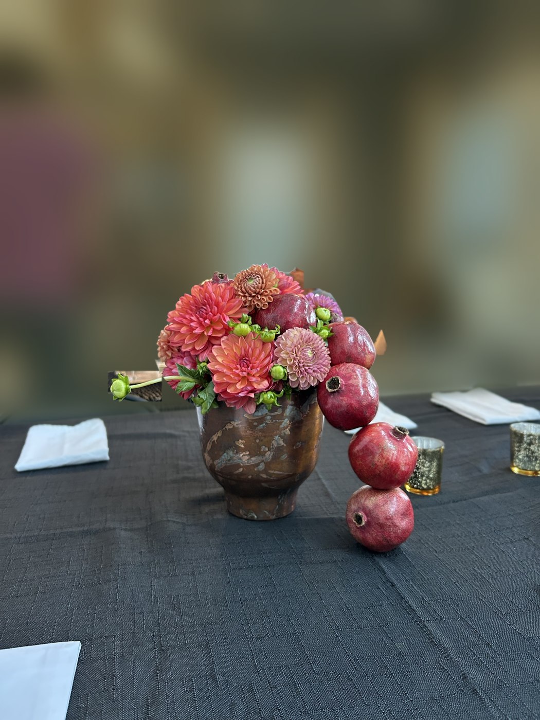Coral and blush dahlias in a bronze vessel, with a column of pomegranates stepping down to the table