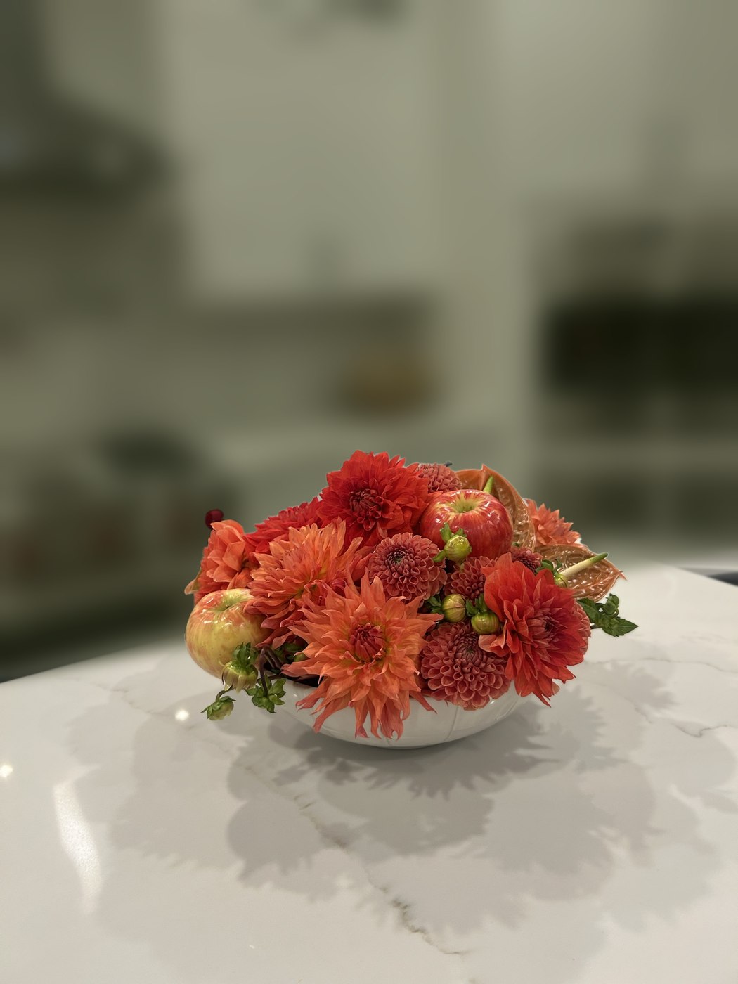 A low white bowl of orange dahlias, apples and peach anthurium