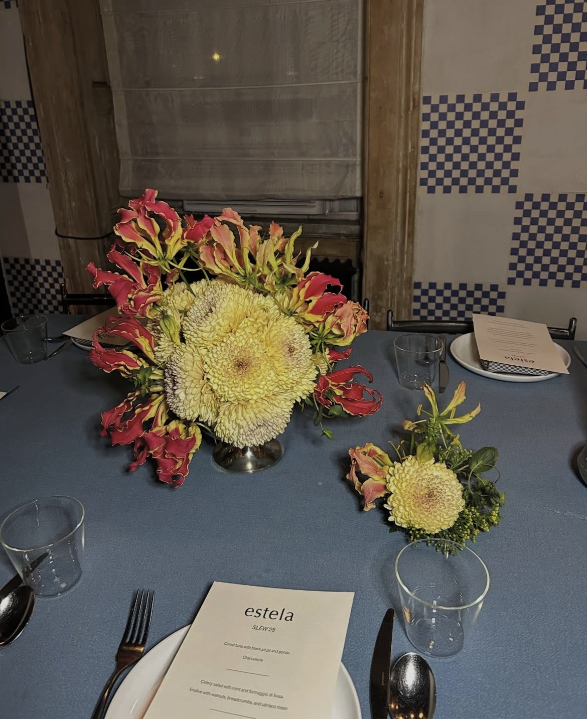 Gloriosa lilies and yellow chrysanthemums in a silver footed vessel on a blue-linen dinner table, with a smaller posy beside it (1 of 3)